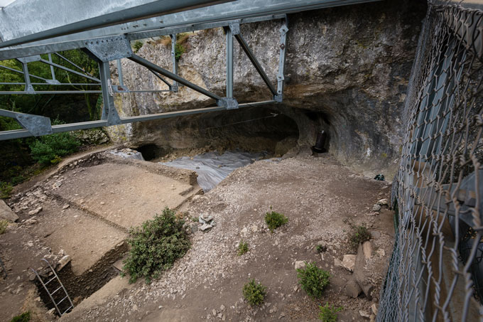 A bird's eye view of a cave behind what appears to be the foundations of a building